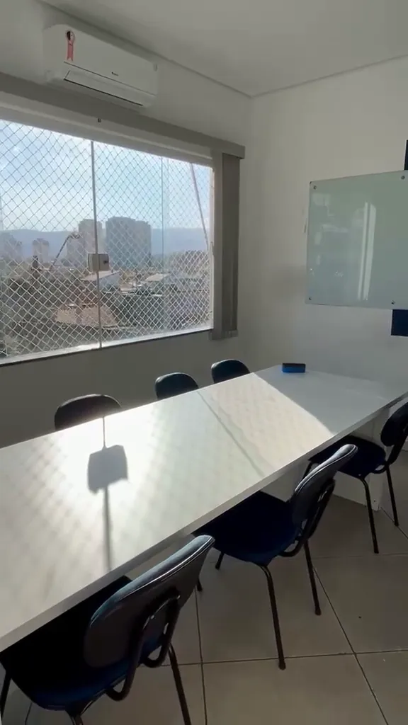 Sala de aula de César de Souza, com mesa branca e a vista da cidade pela janela